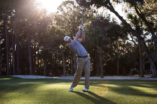 Golfer silhouette with sun backlighting through trees at golden hour